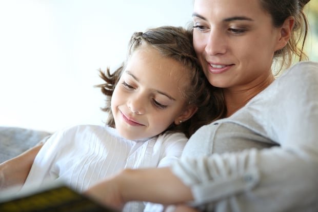 Mom with little girl reading book in sofa