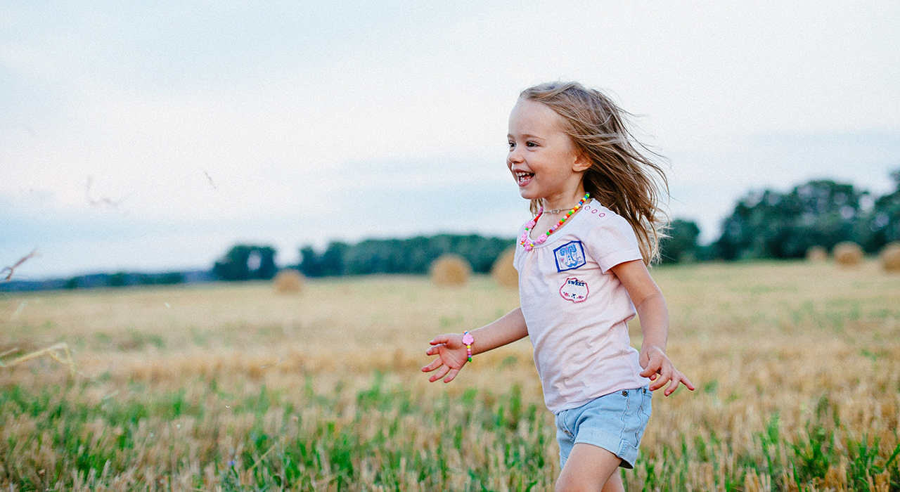 A child running through a field smiling and laughing