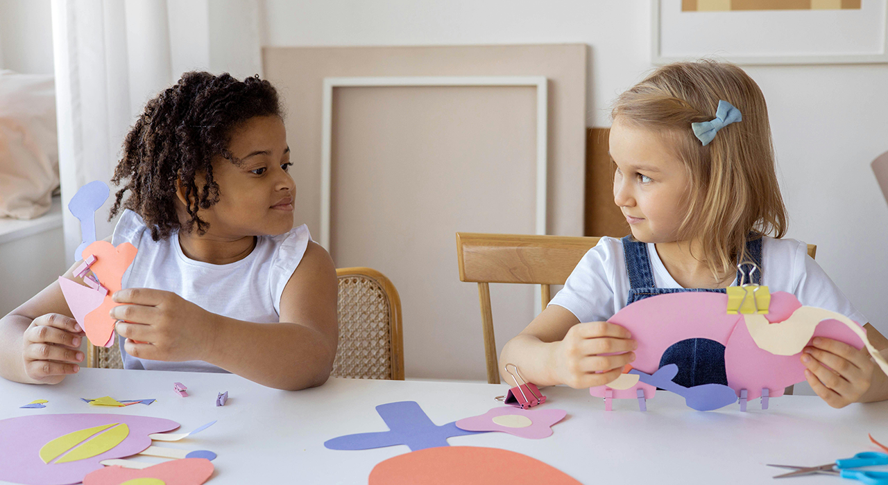 Two children smiling at each other as they engage in a classroom craft activity